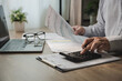 © onephoto - Hands writing on tax document with pen beside laptop on desk, processing financial paperwork for accounting, calculation, expense reporting, and document management in a business workflow