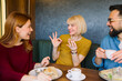 © djile - Happy young adults enjoying meal together while one woman shows approval gesture during casual social gathering