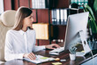 © deagreez - Business woman working at computer in modern office at her desk with documents and keyboard
