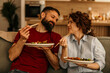 © La Famiglia - Happy couple enjoying takeout food on sofa at home