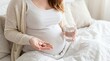 © Eve - Pregnant woman sitting on bed holding glass of water and variety of prenatal vitamin capsules and pills in hand. Pregnancy health, maternity wellness, and prenatal care concept.