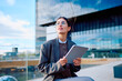 © we.bond.creations - Corporate woman using a digital tablet outdoors, thinking about career growth and ambitions in a modern city environment