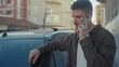 © Krakenimages.com - Young hispanic man holding smartphone to ear, resting his hand on car door and leaning against vehicle on street; concern solitude.