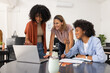 © wavebreak3 - Three female coworkers leaning over laptop displaying documents, pointing and noting in office