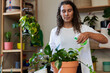 © Wavebreak Media - Nonbinary person misting terracotta pot with green spray bottle in plant room wearing white shirt