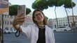 © Krakenimages.com - Woman holding smartphone for selfie on rome street, smiling and looking at screen while wearing glasses and white shirt; city joy.