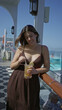 © Krakenimages.com - Woman holding iced cocktail with lemon slice and straw, showing cleavage, leaning on wooden railing of cruise ship terrace under sunny sky; relaxation.