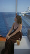 © Krakenimages.com - Woman smiling and sitting showing cleavage on cruise ship terrace with ocean view and drink nearby; relaxed serenity.