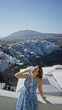© Krakenimages.com - Woman raising arm with sunglasses on a white building terrace, leaning on a wall and smiling at the view; vacation serenity.