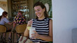 © Krakenimages.com - Young brunette woman sipping a creamy pineapple cocktail while holding a straw at a bar table with wicker stools and tile wall, smiling; happiness.