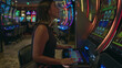 © Krakenimages.com - Woman young hispanic brunette playing slot machines with hands pressing buttons while seated and leaning on chair at casino; anticipation risk chance.