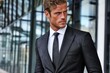 © whitestorm - A handsome man with curly blonde hair and blue eyes wearing a sharp dark suit and tie, looking confidently to the side.