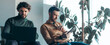 © Prostock-studio - Two men are engaged in work activity in a contemporary office. One man uses a laptop while the other interacts with a tablet. Both appear focused on their tasks in a bright, green environment.