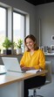 © Alexander Chaykin - Woman wearing yellow top sitting at desk using laptop. Modern office with natural light, plants and chairs.