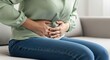 © twilight mist - Woman experiences severe abdominal pain while sitting on a couch.