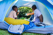 © Wavebreak Media - African adult, youth males in blue tent sipping mugs, sunlight causing adult extending mug outward