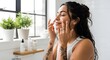 © Andres Mejia - Beautiful Young Woman Applying Skincare Product to Her Face with Eyes Closed, Enjoying a Relaxing Self-Care Beauty Routine