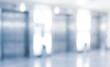 © birulaut - A blurred view of an elevator lobby in a modern building, showcasing reflective metal elevator doors and a bright, well-lit environment.