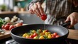 © The Little Hut - Hand adding cherry tomatoes to a frying pan with herbs, cooking a healthy meal in a modern kitchen