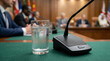 © Andrey - Microphone and glass of water on green table at global wealth summit with international flags in blurred background