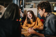 © qunica.com - Students sit around a table smiling and talking while studying together. A casual group of young friends engages in a relaxed conversation and collaborative study session.