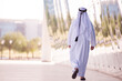 © .shock - Man in white thobe walking by reflective modern building facade in an urban setting