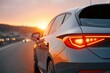 © DSimage - Modern car driving on highway at sunset with red tail lights glowing and warm sunlight reflecting on the rear bodywork