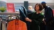 © DC Studio - Woman customer looks through clothes hanging on racks, searching for black friday special offers in trendy clothing boutique. Shopper holding items with discount red sale price tags.