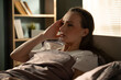 © Grustock - Young woman lying in bed at dawn, pressing temples in pain and grimacing from a severe headache or migraine, morning light filtering into a quiet bedroom scene
