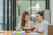 © Songsak C - Two Asian businesswomen collaborating and discussing financial project on laptop and documents in office.