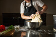 © Taras Grebinets - Home Baker Kneading Dough in Kitchen With Apron and Stainless Steel Mixing Bowl