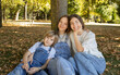 © Anna - happy mother with two children of different ages, a teenage daughter and a teenage son, sit together on the grass in a park. Concept of a happy, close-knit family. Maternal love. Mother's Day