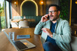 © djile - Businessman having phone call while working on laptop in cafe