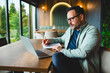 © djile - Focused businessman writing notes while working on laptop in cafe