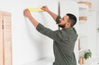 © Pixel-Shot - Young man applying masking tape to white wall at home