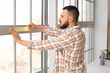 © Pixel-Shot - Young man applying masking tape to window at home