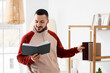 © Pixel-Shot - Handsome young man reading book near bookshelf at home