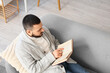 © Pixel-Shot - Handsome young man reading book on grey sofa at home
