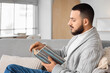 © Pixel-Shot - Handsome young man reading book on grey sofa at home