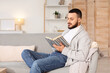 © Pixel-Shot - Handsome young man reading book on grey sofa at home