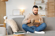 © Pixel-Shot - Handsome young man with cup of tea reading book on grey sofa at home