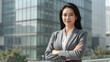 © NAD SANG PAP - Confident businesswoman in gray suit standing with arms crossed outdoors near modern office building, smiling with professional and approachable expression in urban environment