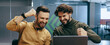 © Prostock-studio - Two men sit in an office, smiling and celebrating as they look at a laptop screen. They show enthusiasm and joy in the moment.