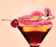 © New Africa - Attractive woman with swim ring in glass of cocktail against pink beige background