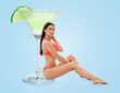 © New Africa - Attractive woman in swimsuit sitting next to glass of cocktail against light blue background
