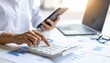 © Khasani - Close-up of hands using a calculator and smartphone, with a laptop and glasses in the background, symbolizing financial planning and analysis