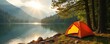 © Viktor - Orange tent pitched near calm lake water by forest trees. Mountains rise in background bathed in bright sun rays. Nature scene perfect for outdoor adventure and peaceful retreat.