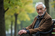 © Maryna - Old man with white hair sits alone on park bench outdoors. He looks thoughtful and contemplative. Autumn trees are blurred in the background. Copy space is available.