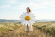 © Breezze - Serene woman holding oversized chamomile flower standing in a field for skincare branding and spa advertising with copy space and a soft horizon background