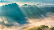 © huythoai - A breathtaking sunrise over mist-covered mountains, where golden sun rays stream through layers of fog and illuminate rolling green hills. In the foreground, terraced farmland and greenhouse structure